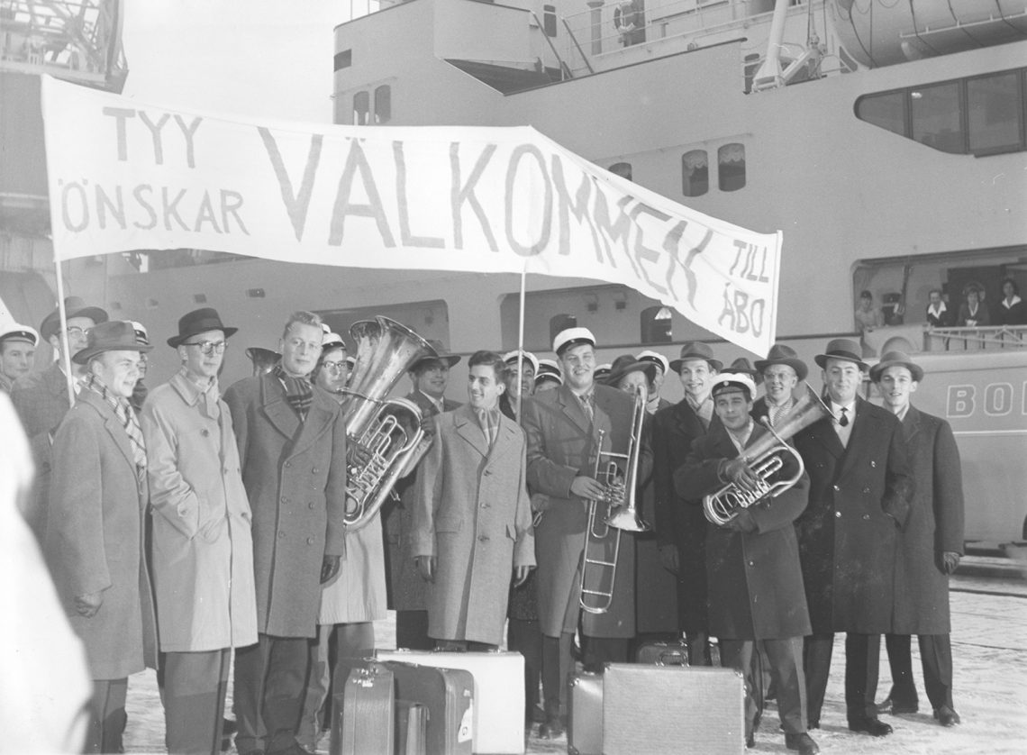 mv-kuvassa ylioppilaskunnan jäseniä satamassa torvien ja "Välkommen" banderollin kanssa.