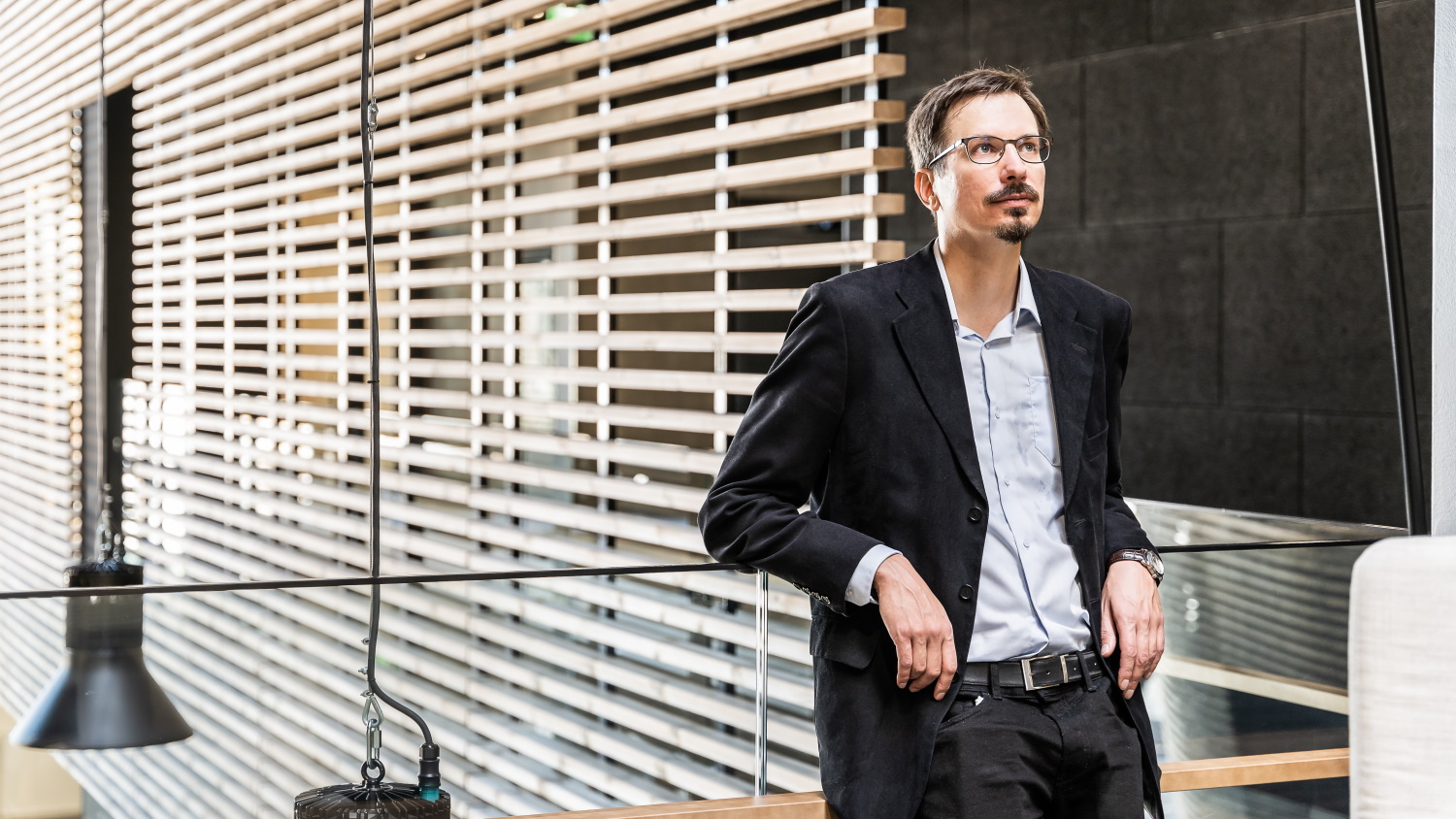 Pekka Peljo nojaa lasiseen kaiteeseen ja katselee yläviistoon.