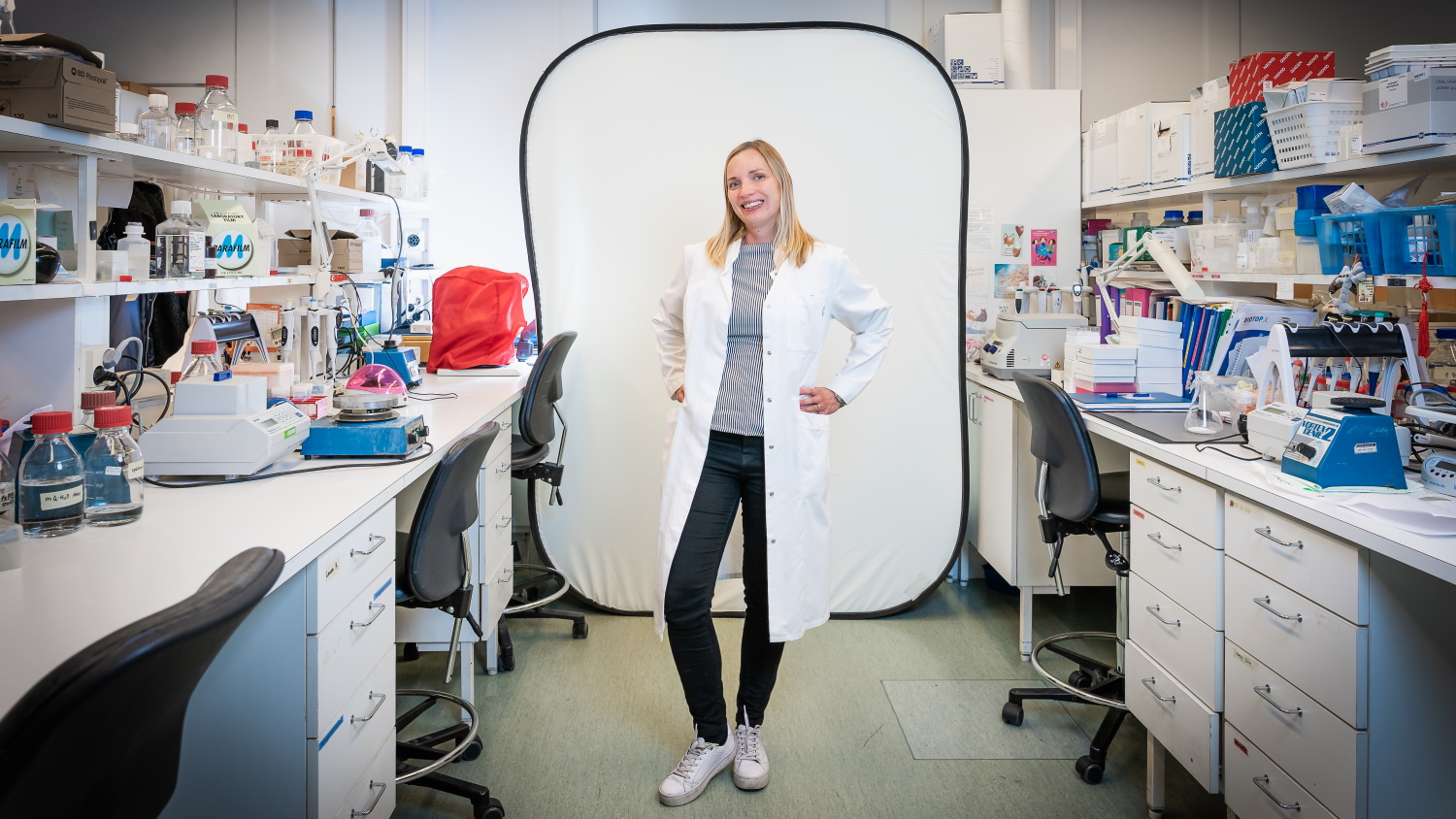 Maija Hollmén seisoo laboratoriossa ja katsoo kameraan.